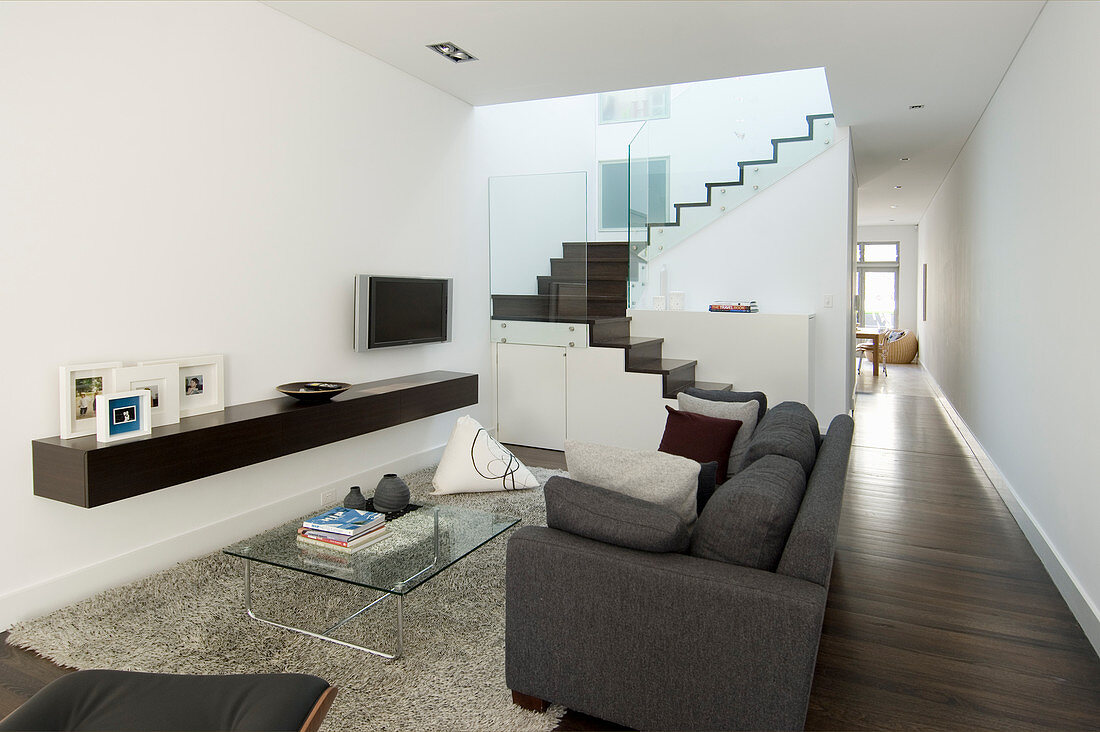 Sofa, glass table and floating shelf in living room and staircase with glass balustrade in background