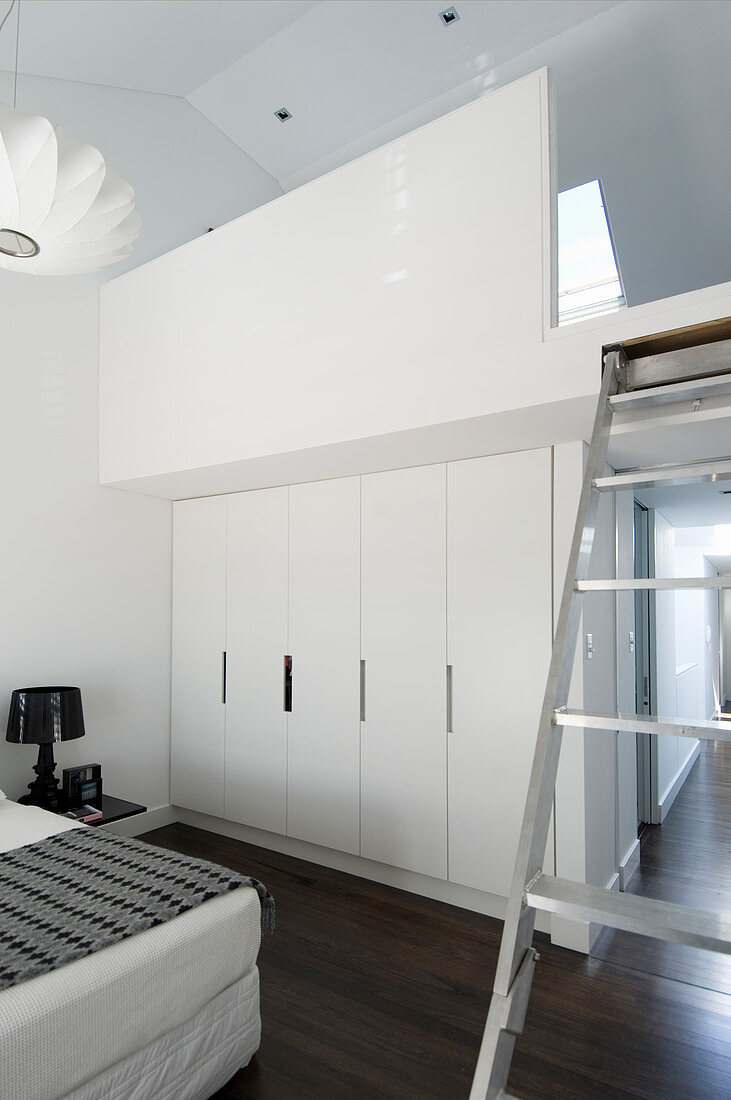 White fitted wardrobes below gallery accessed by ladder in white bedroom