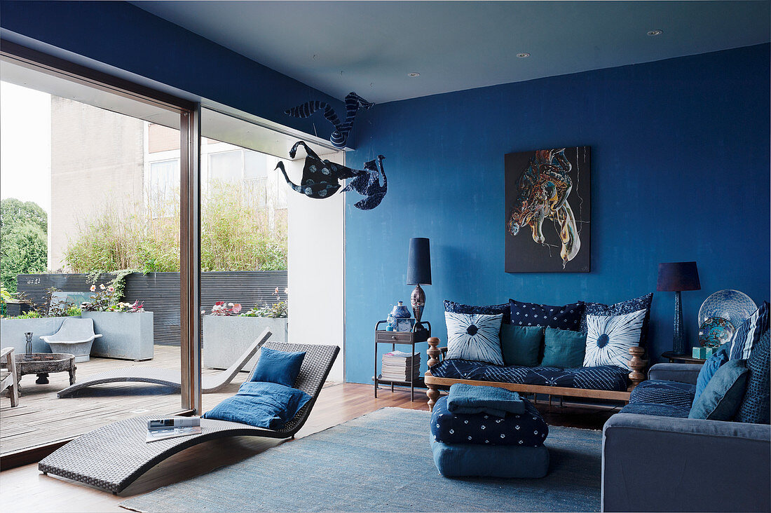 Blaues Wohnzimmer mit verschiedenen Sitzmöbeln und Liege vor Glasschiebetür