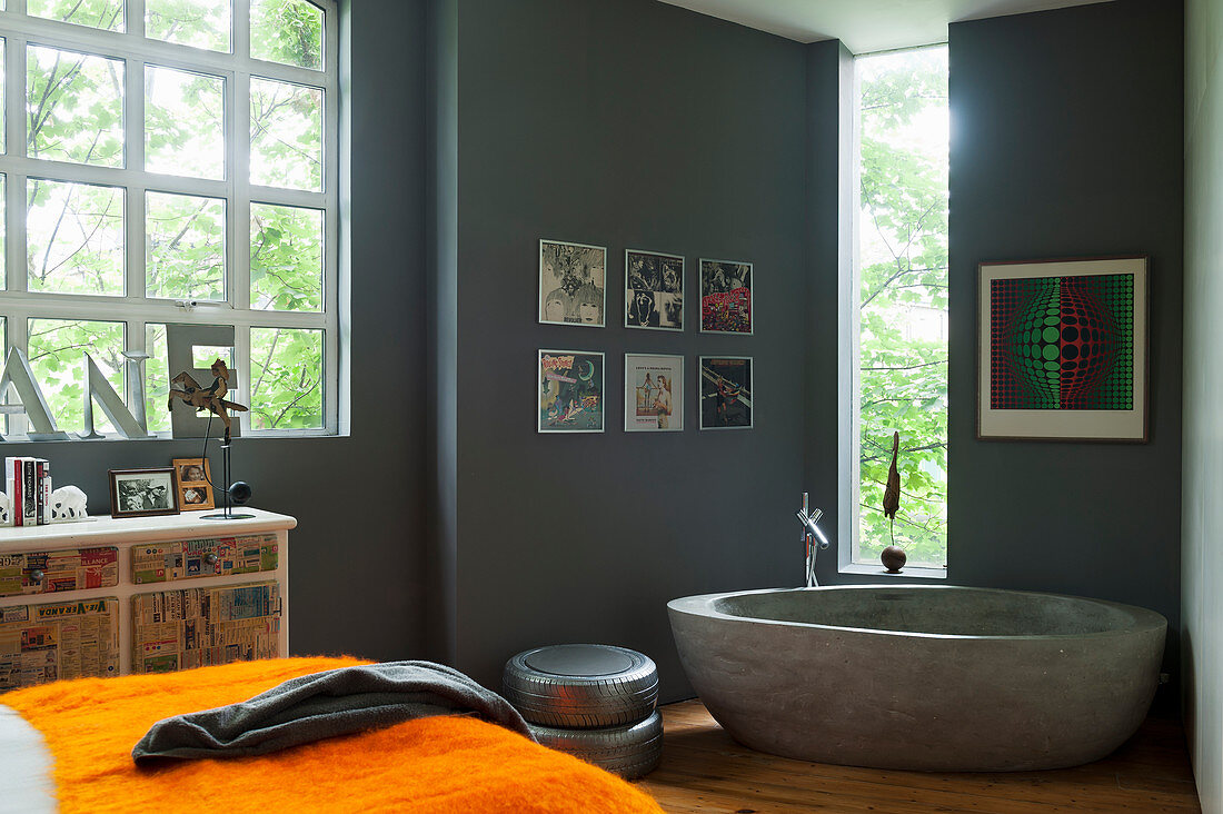 Free-standing concrete bathtub in bathroom with grey walls decorated with framed record covers an, industrial window