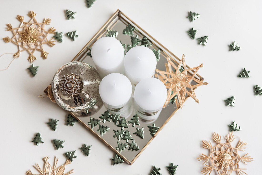 DIY Advent arrangement of candles, bauble, scattered decorations and straw stars on mirrored tray