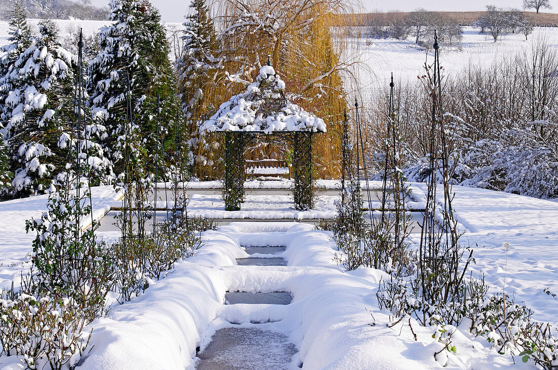 Verschneiter Garten im Winter mit zugefrorenem Teich und Pavillon