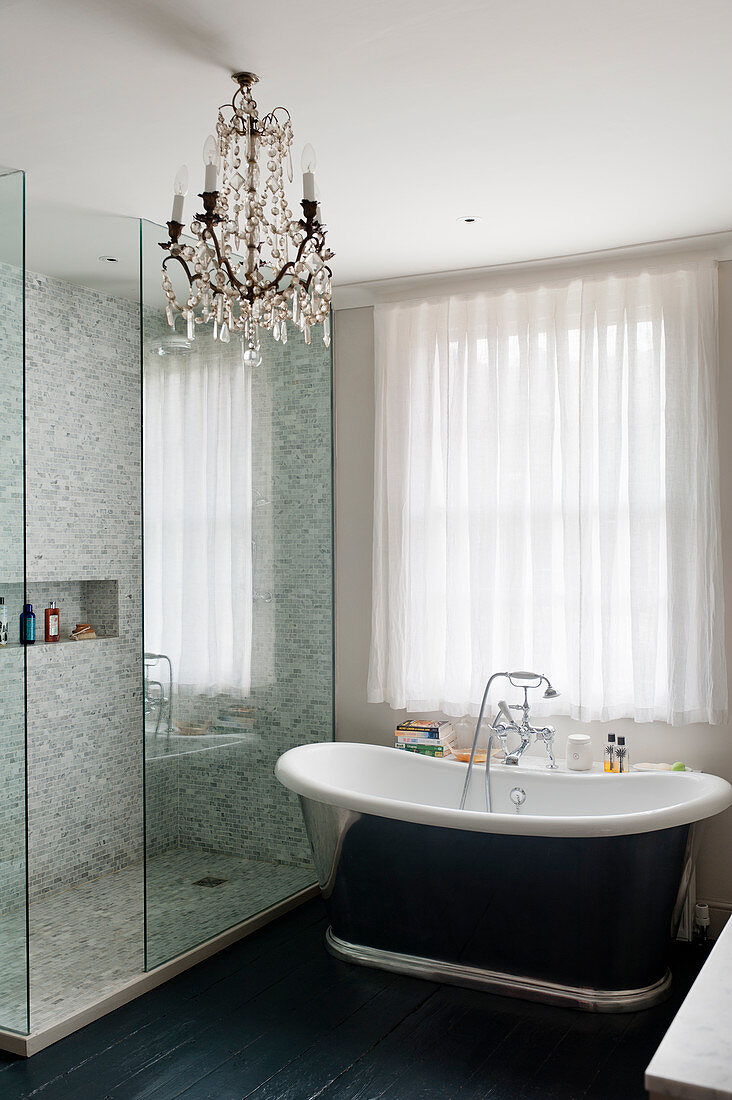 Roll-top bath in bathroom with mosaic tiles and glass chandelier