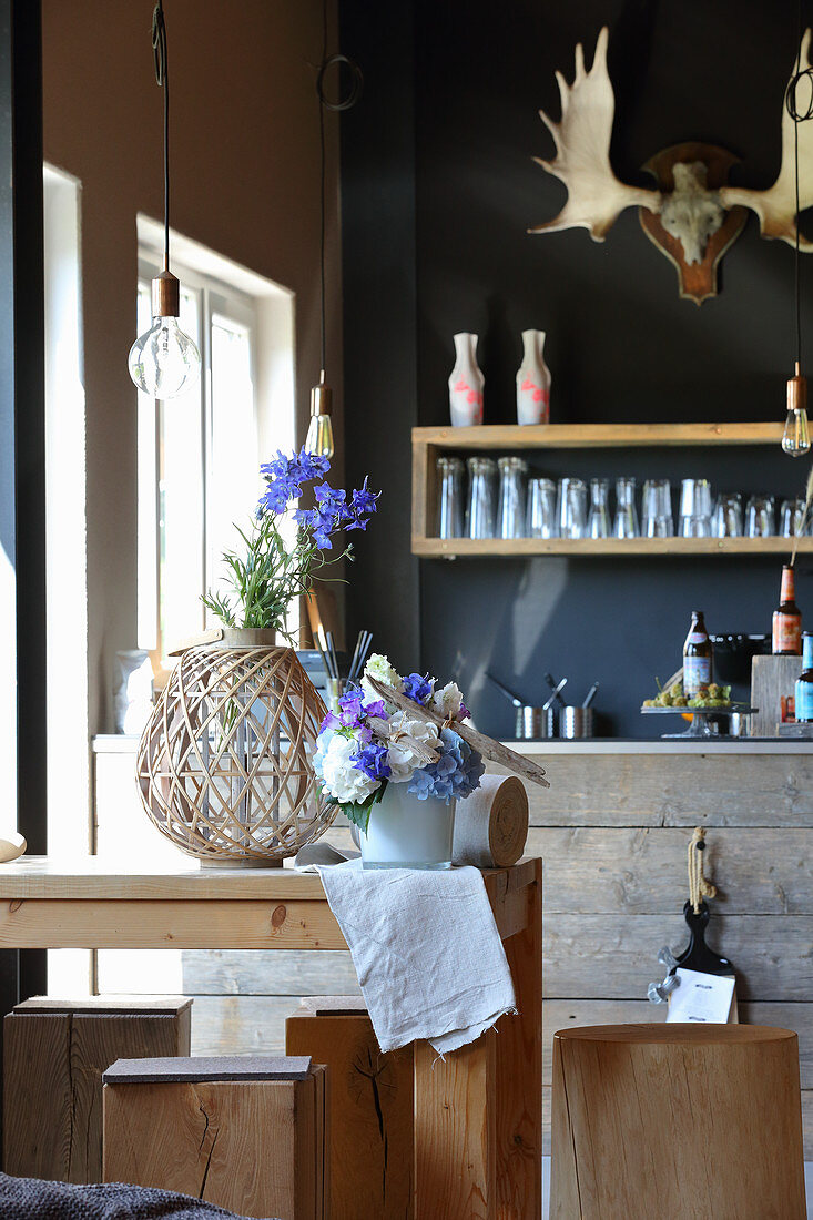 Rittersporn in Vase und DIY-Blumenschmuck mit Treibhölzern auf Tisch in Küche