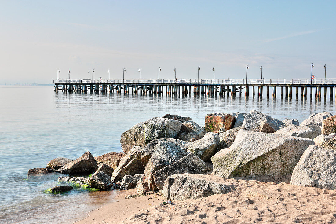 View across pile of boulders on beach to pier stretching out into sea
