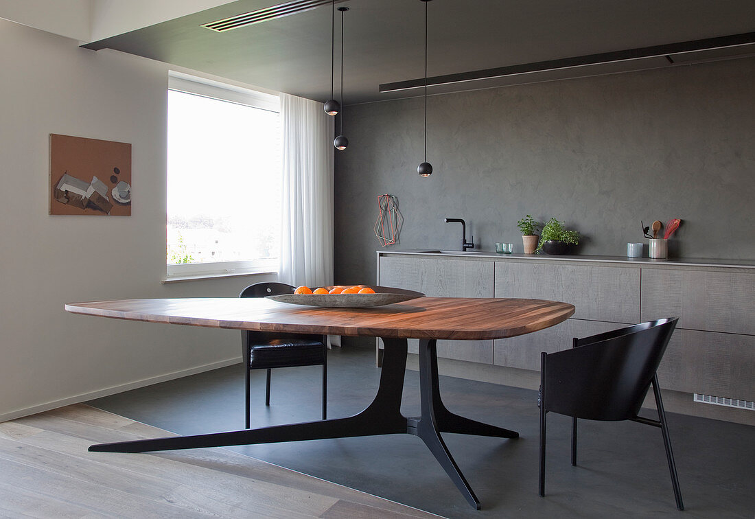 Designertisch mit Holzplatte, schwarze Schalenstühle in offener Küche mit grauer Wand
