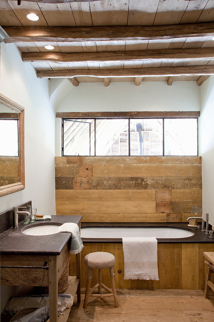 Wood-clad bathtub below window in rustic bathroom