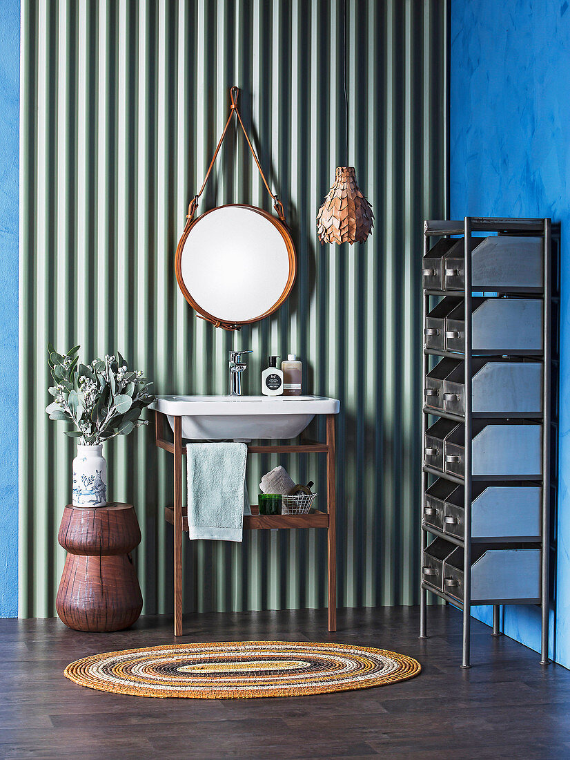 Vanity stand and round mirror on corrugated iron panel, metal shelf on the side with school baths on a blue wall