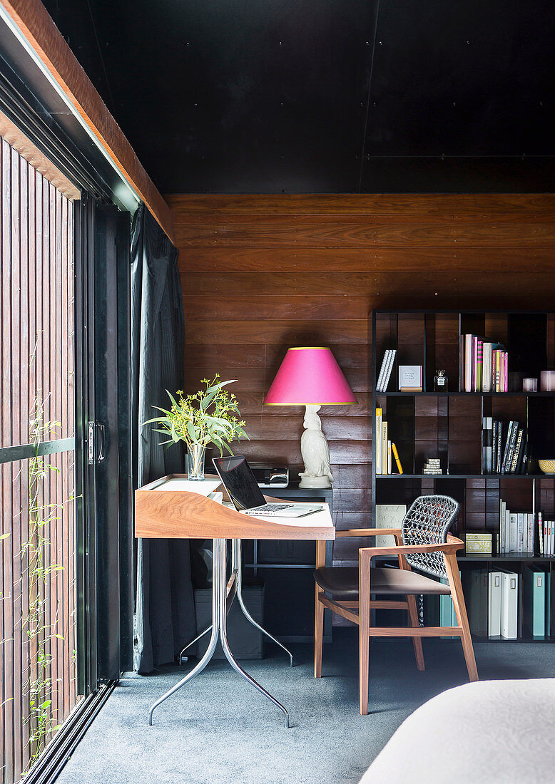 Desk by the window against a wall with wood paneling