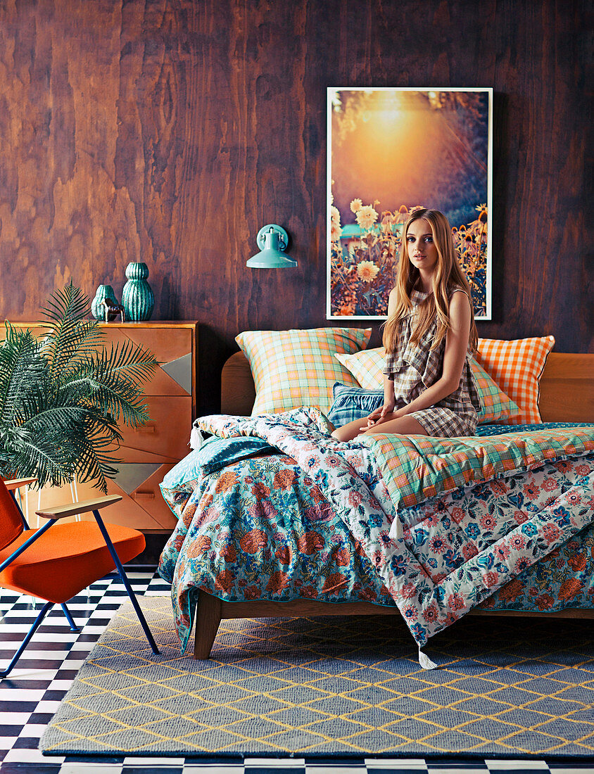 Junge Frau auf Doppelbett mit bunter Bettwäsche vor Holzwand