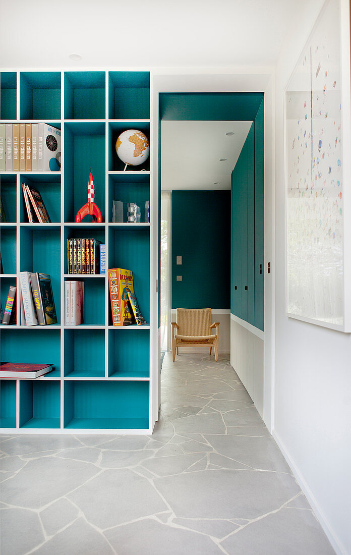Turquoise fitted shelving next to open doorway leading into adjoining room with continuous stone floor
