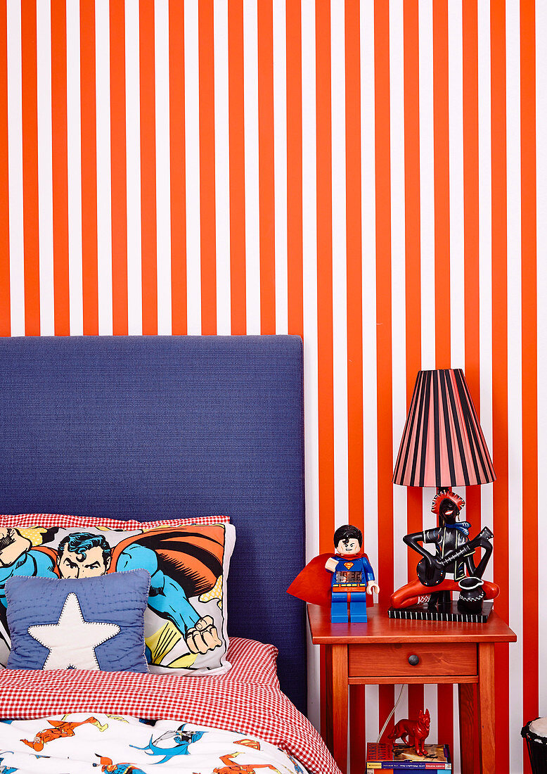Bed with comic sheets and bedside table in front of striped wallpaper in boy's room