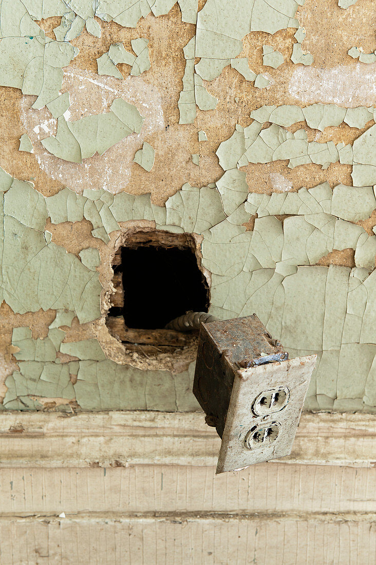 Old power socket hanging out of wall with peeling paint