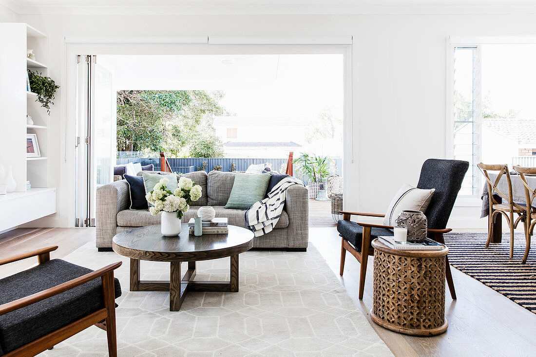 Gray upholstered sofa with cushions, round coffee table, armchair and side table in front of an open patio door in a bright living room