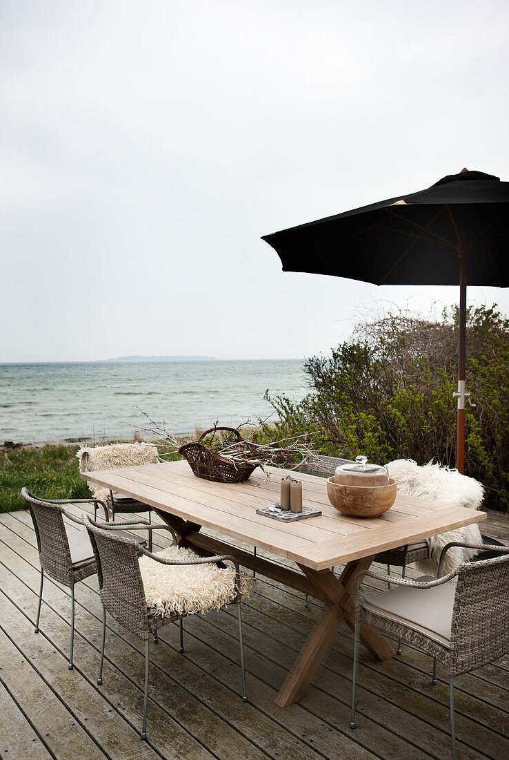 Holztisch und Stühle mit Fellen auf der Terrasse mit Blick aufs Meer