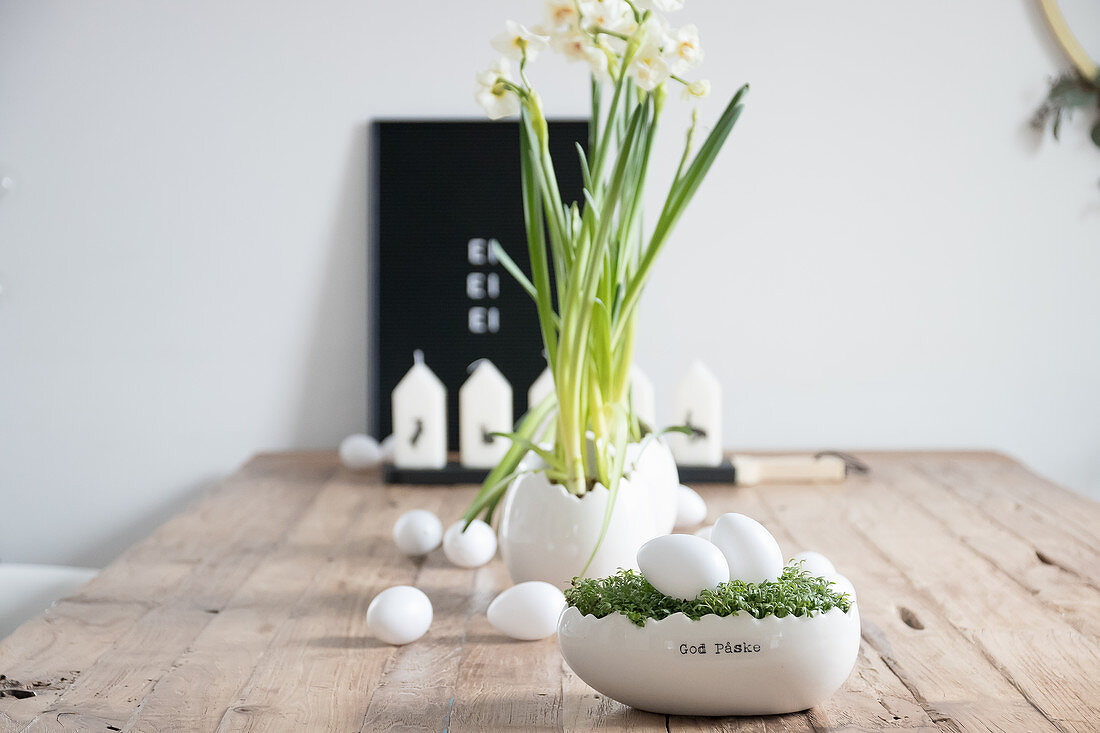 Holztisch mit Osterdekoration: Kresse-Nest mit weißen Eiern, Narzissen und Kerzen
