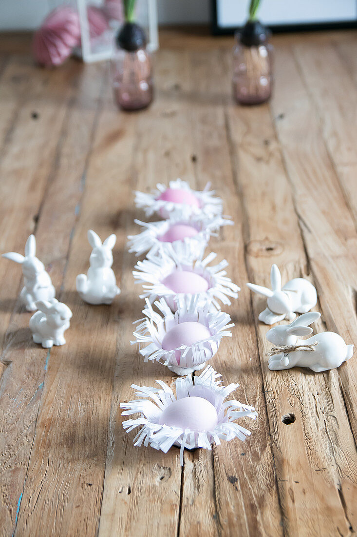 DIY-Papiernester mit Ostereiern und Hasenfiguren auf Holzuntergrund