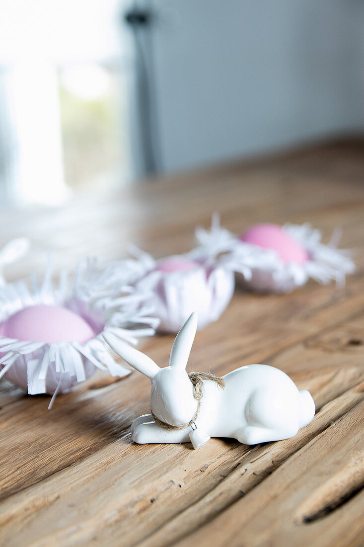 Bunny figurines and Easter eggs in handmade paper nests on wooden surface