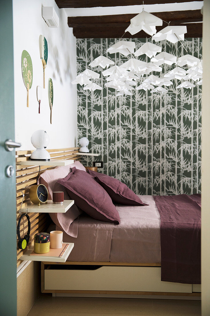Blick auf Doppelbett mit Bettwäsche in Beerentönen, grau-grüne Tapete und Mobile