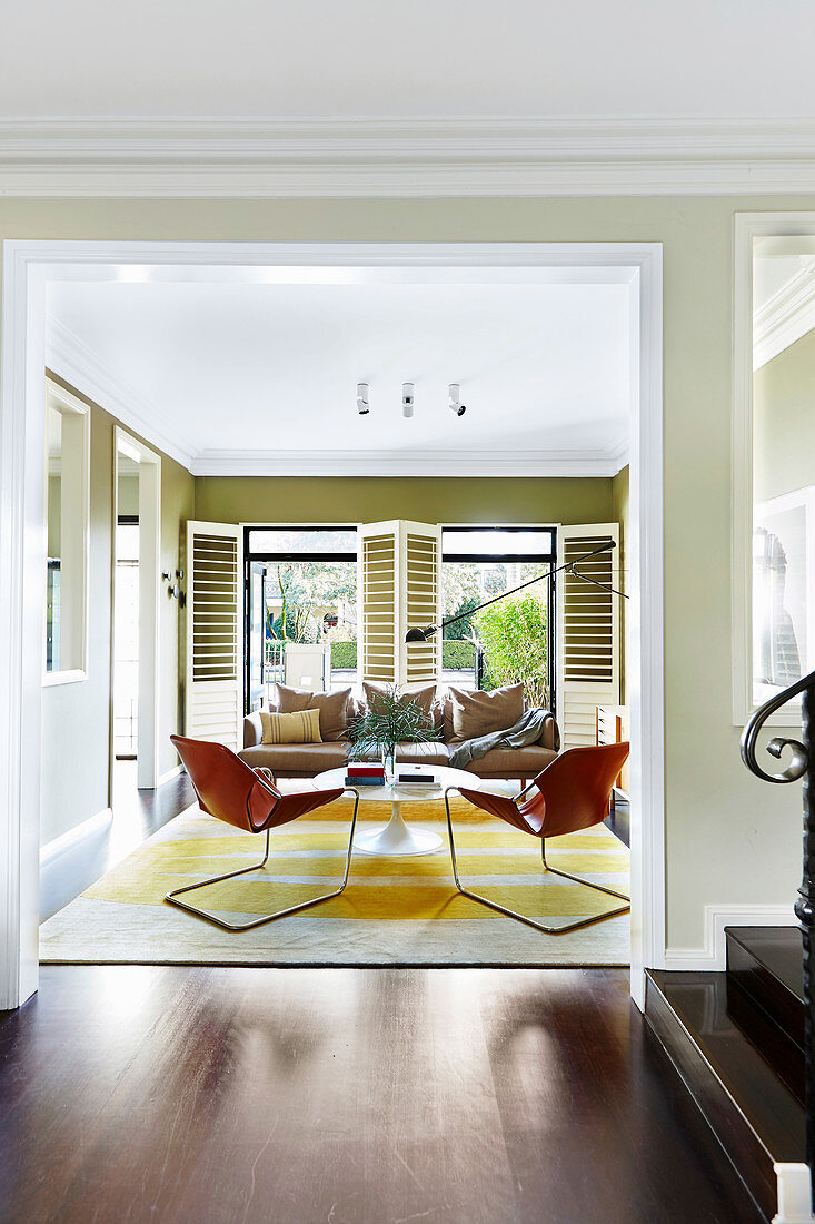 Blick in Wohnzimmer mit cognacfarbenen Lederstühlen, Klassikertisch und Sofa vor Terrassentür