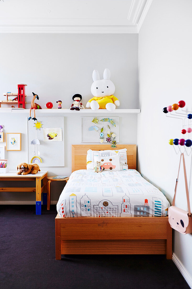 Holzbett mit bunter Bettwäsche, darüber Regal mit Spielfiguren im Kinderzimmer