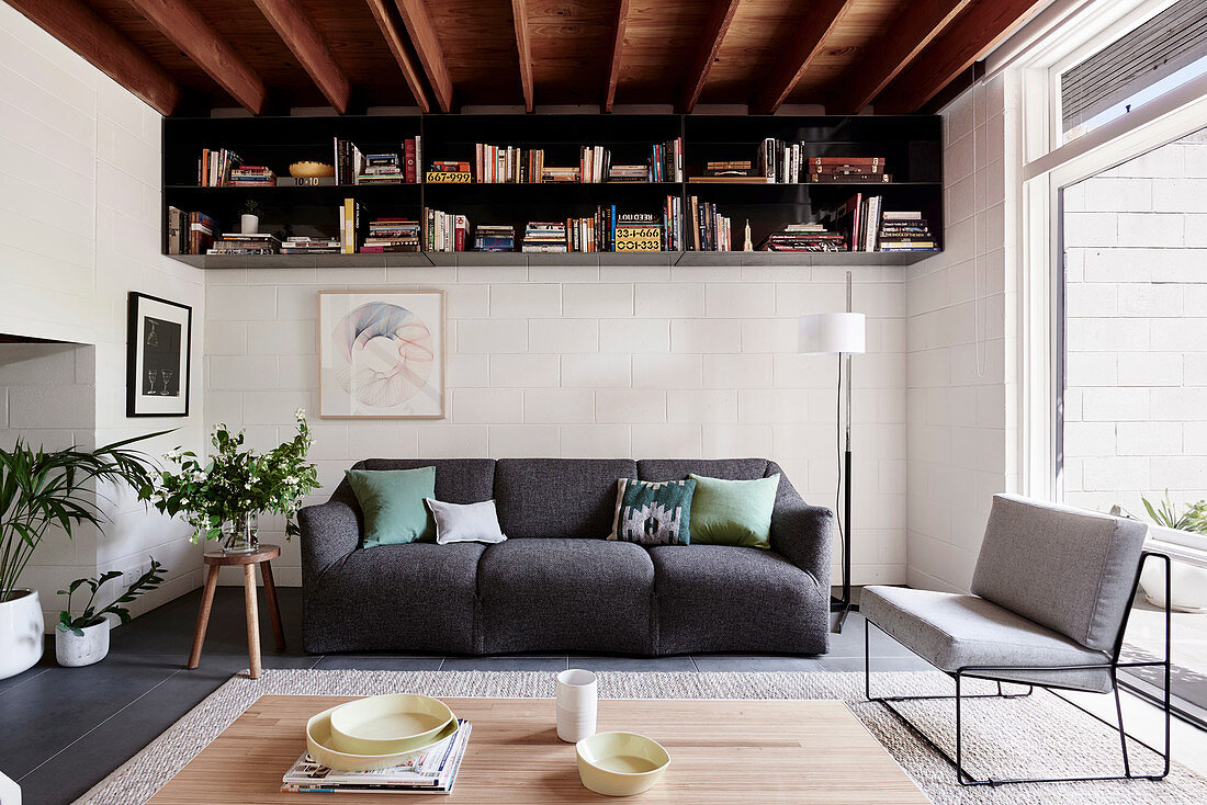 Gray upholstered sofa, bookshelf above in the living room with wooden beam ceiling