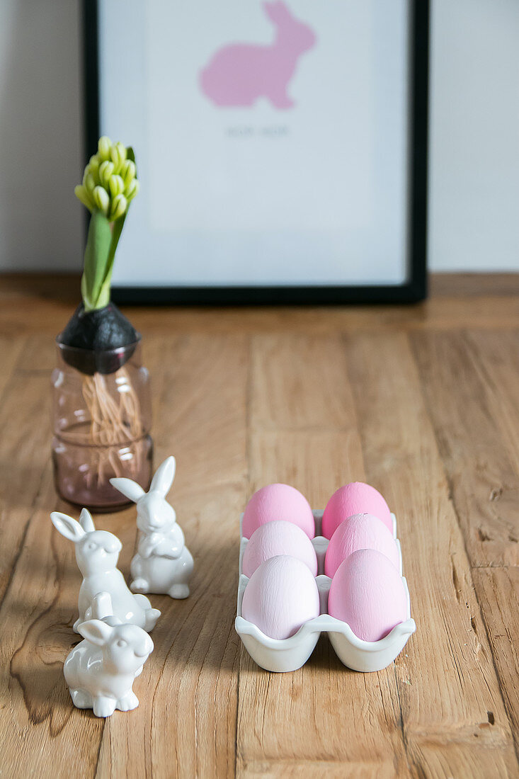 Pink eggs in egg rack, bunny figurines and hyacinth on wooden table
