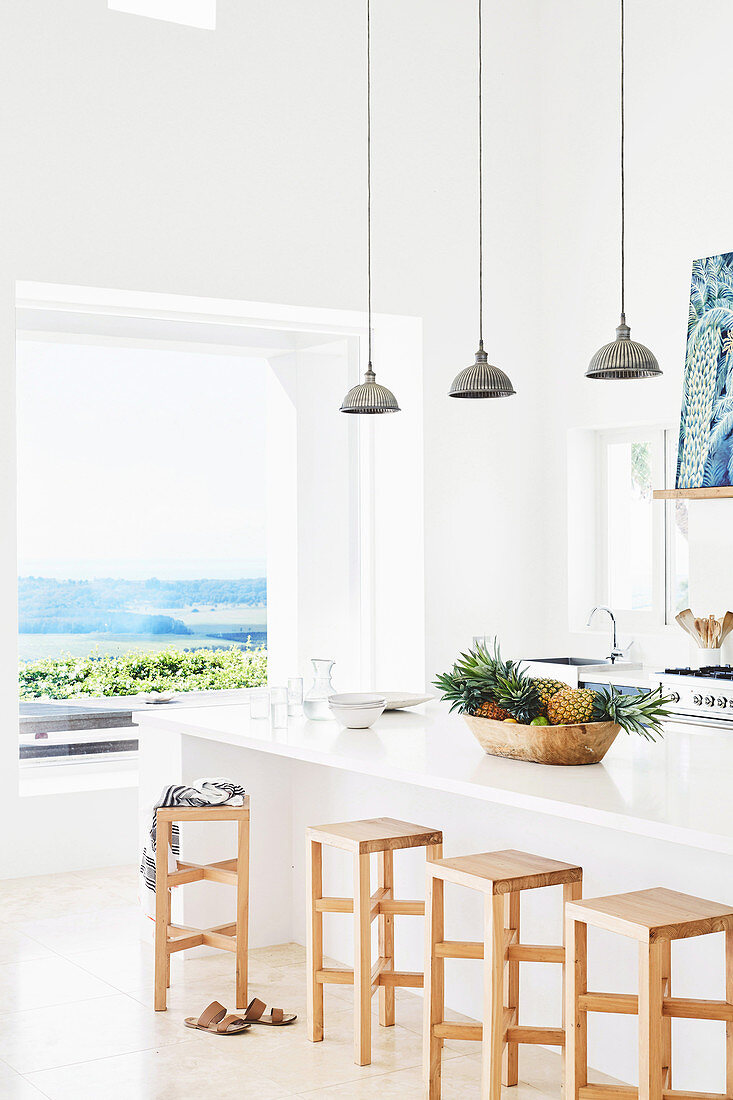 Küchentheke mit Barhopckern aus Holz und Pendelleuchten im Hintergrund Fenster mit Meerblick