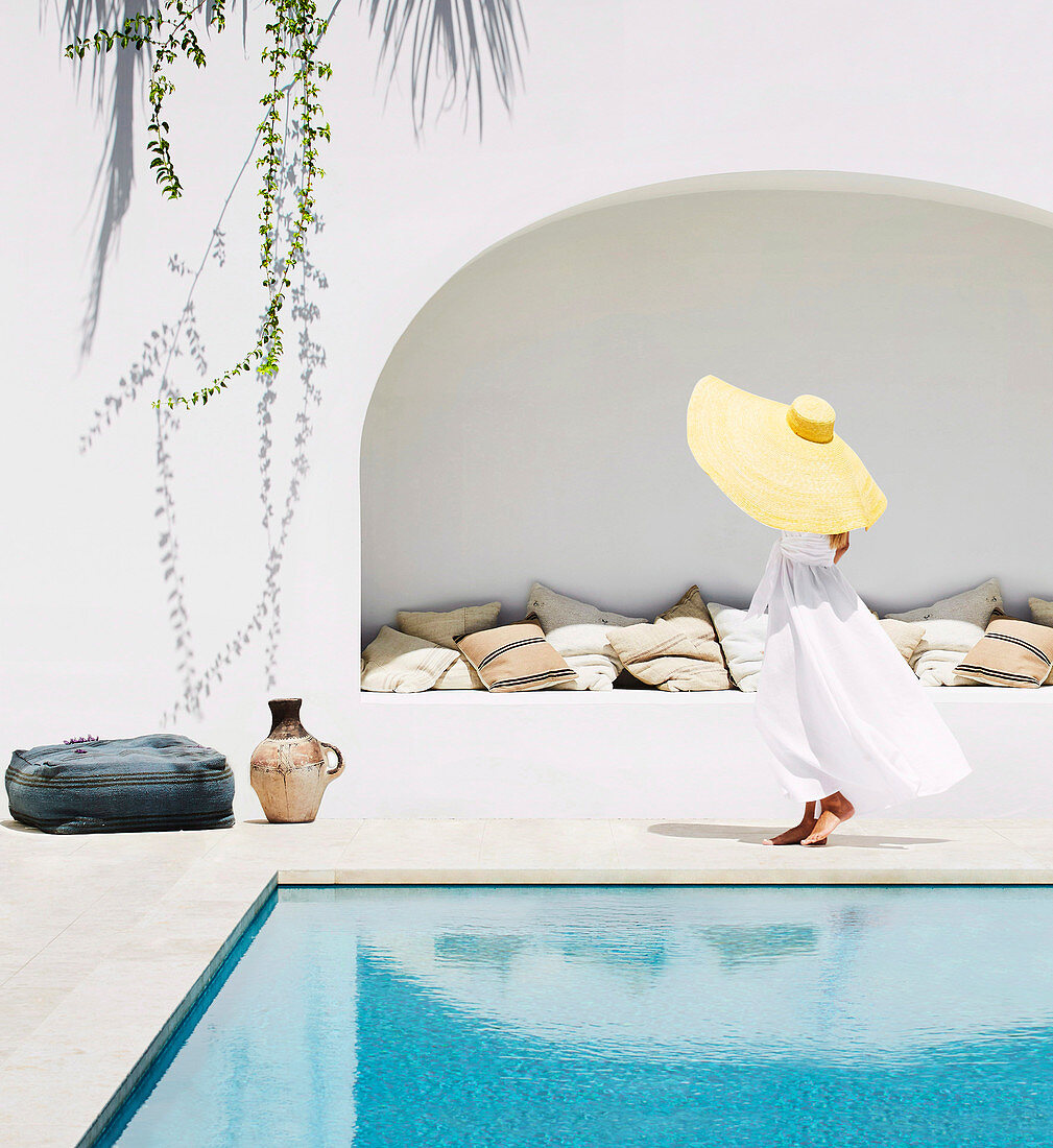Woman with hat in white dress by the pool