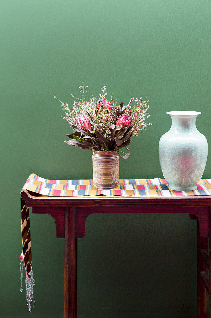 Konsole mit Tischläufer, Vase und Blumenstrauß vor grüne Wand