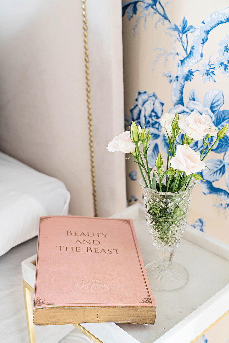 Book and vase of flowers on bedside table against blue-and-white floral wallpaper