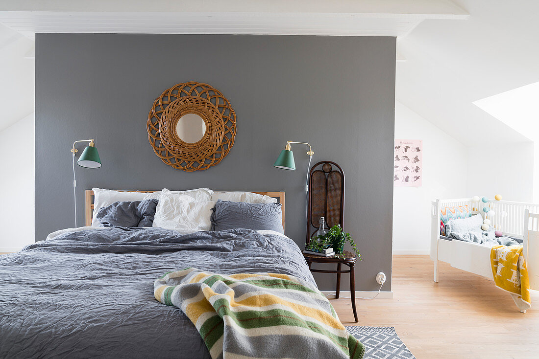 Bett vor grauer Wand im hellen Schlafzimmer mit Kinderbett