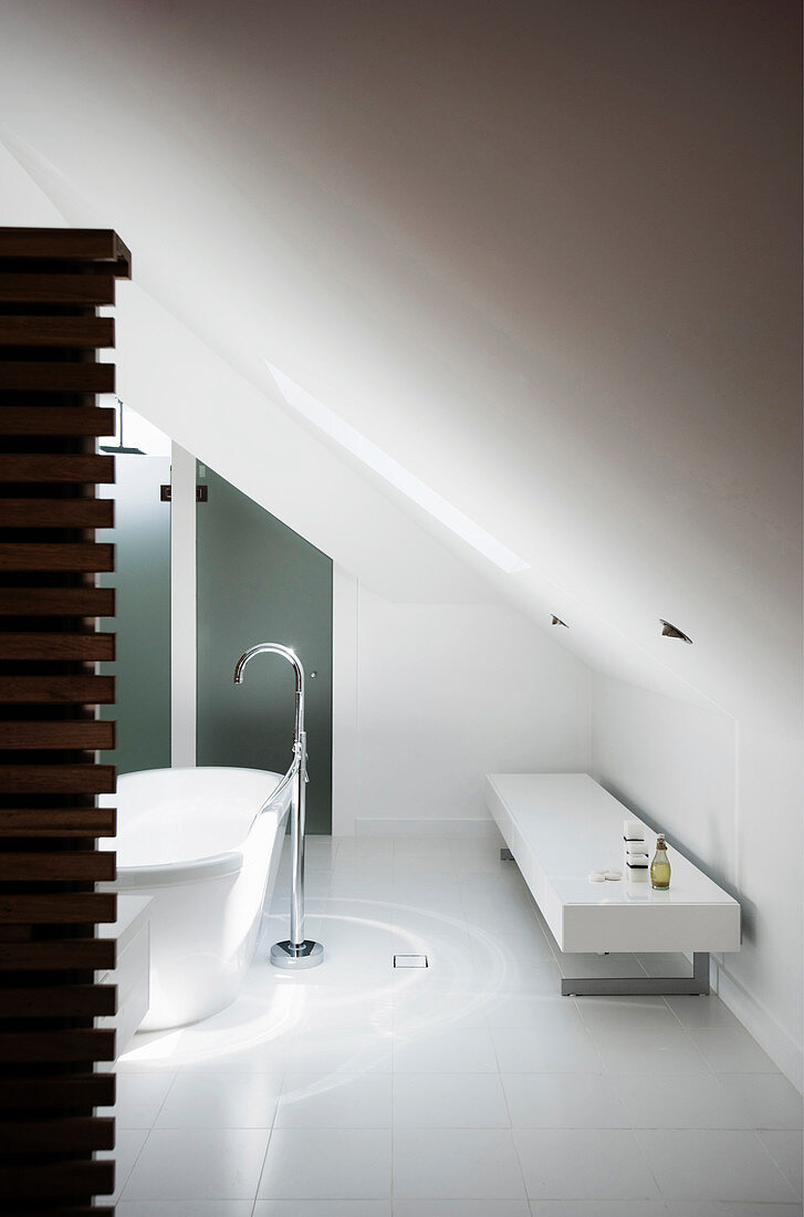 Free-standing bathtub with floor-mounted taps and bench in white designer bathroom with sloping ceiling