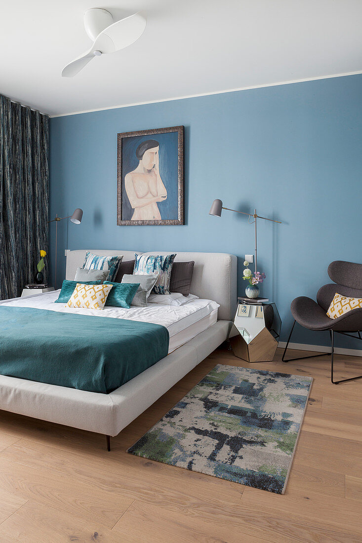 Doppelbett, daneben verspiegelter Nachttisch und Designerstuhl im Schlafzimmer mit blauer Wand