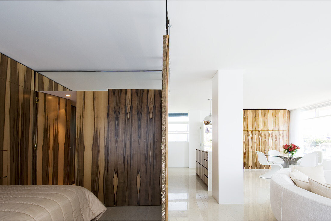 Schlafbereich mit Holzschiebeelement, im Hintergrund weißes Designersofa und Essbereich