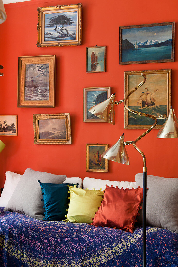 A collection of painted seascapes on red wall above day bed, the floor lamp is 1940s
