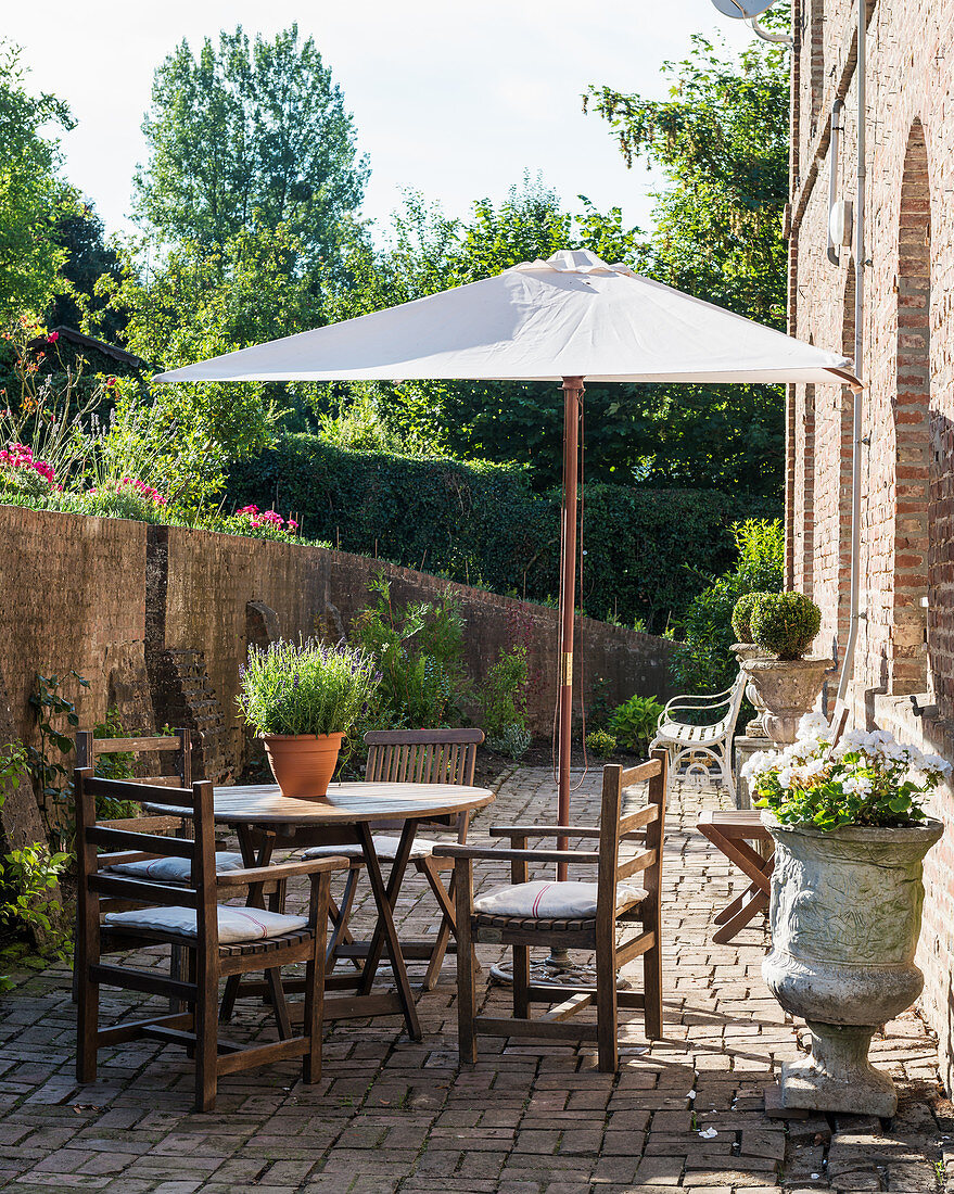 Teak furniture and stone urns on sunny bricked terrace with parasol
