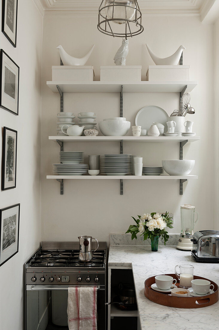 Crockery on shelves on wall above cooker and worksurface in corner of kitchen