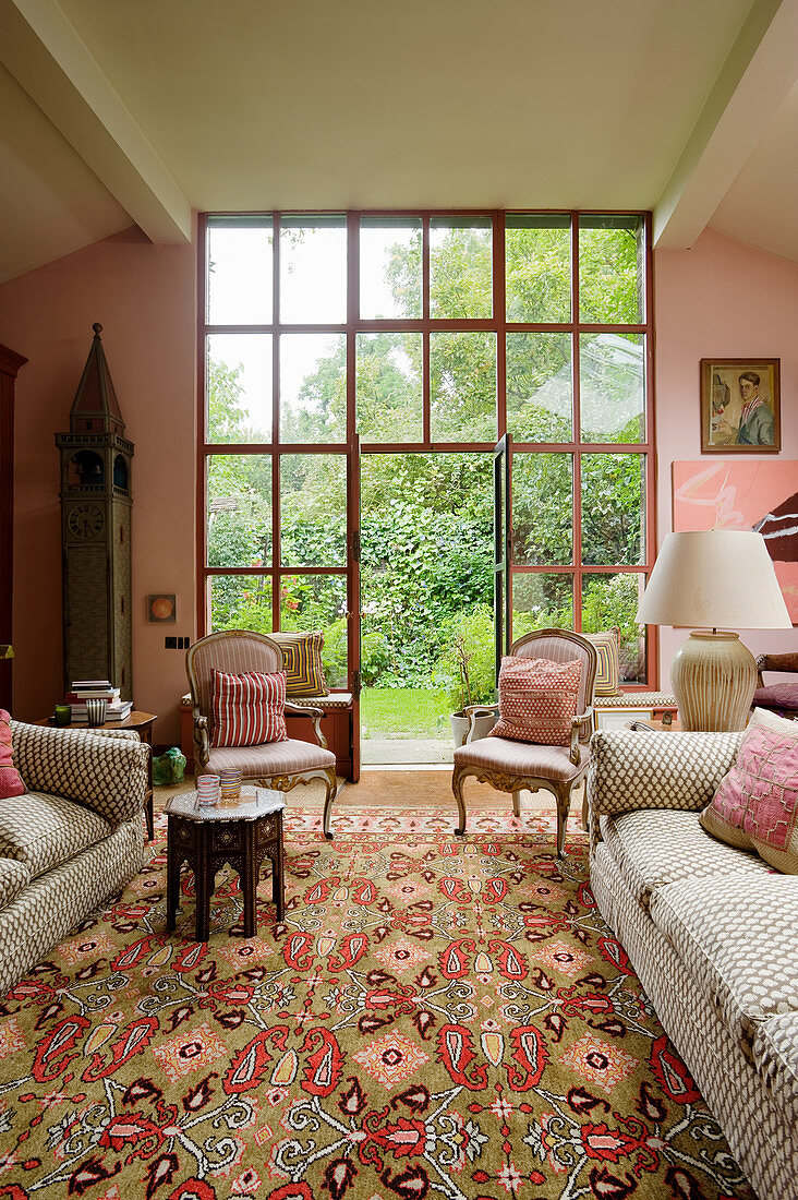 Wohnzimmer in Rosatönen mit Couch und antiken Polsterstühlen vor raumhoher Fensterfront zum Garten
