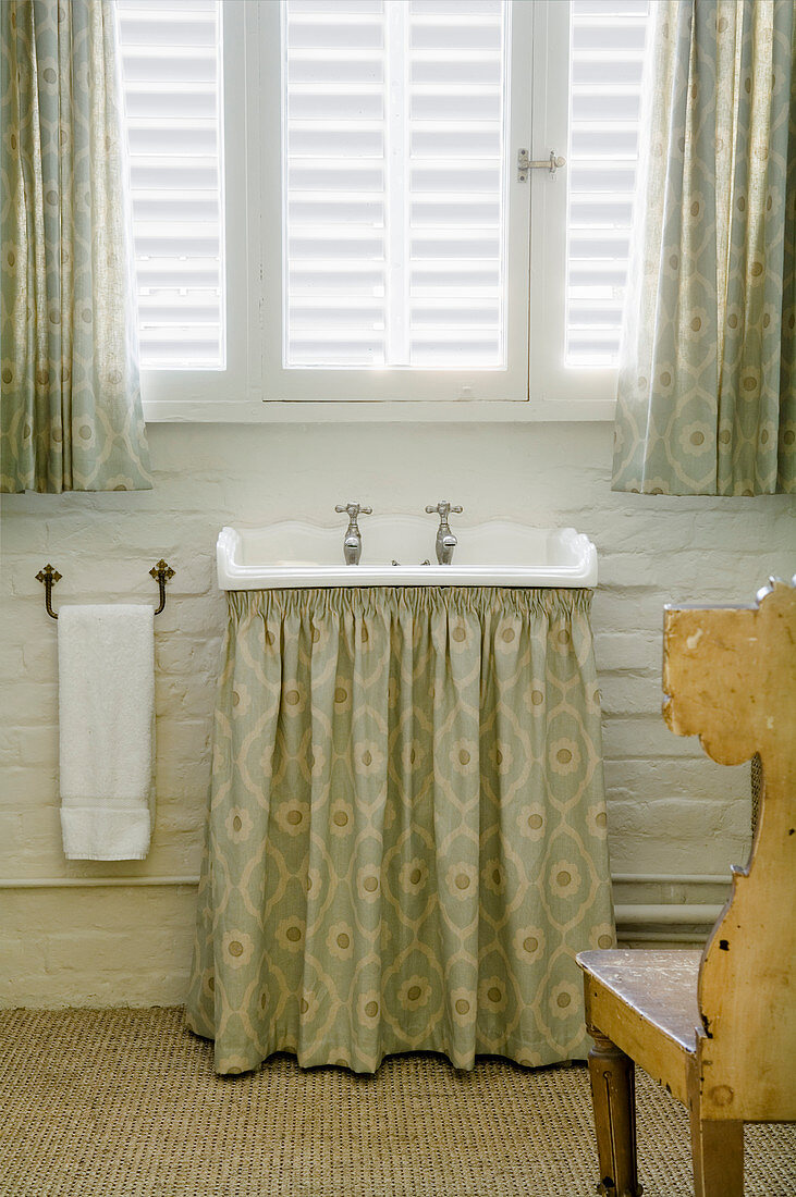Antique sink with green, patterned curtain below under window