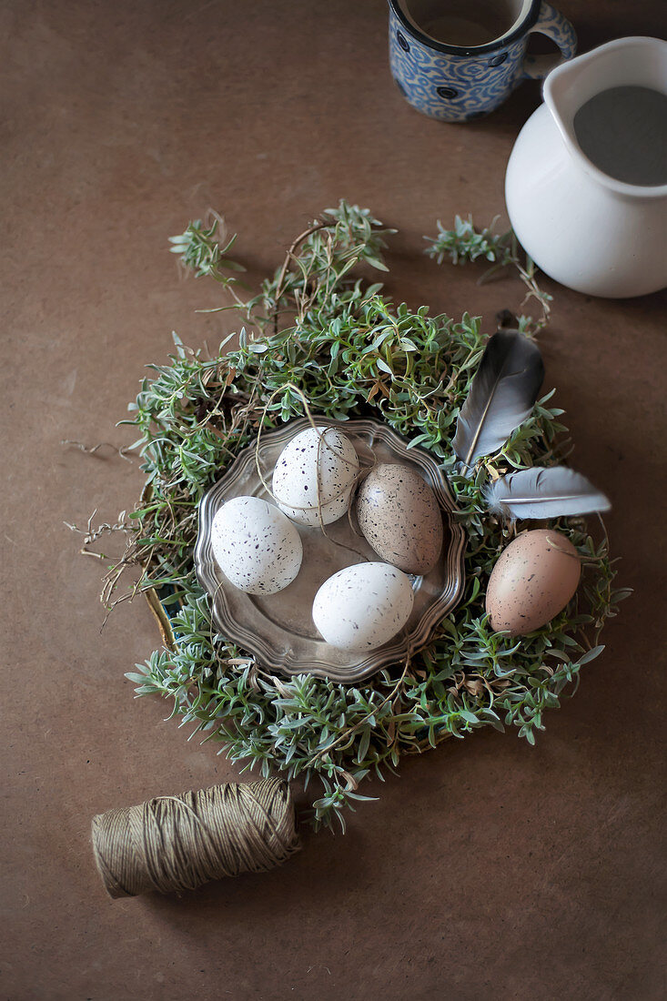 Besprenkelte Eier auf Zinnteller im Osternest mit Federn