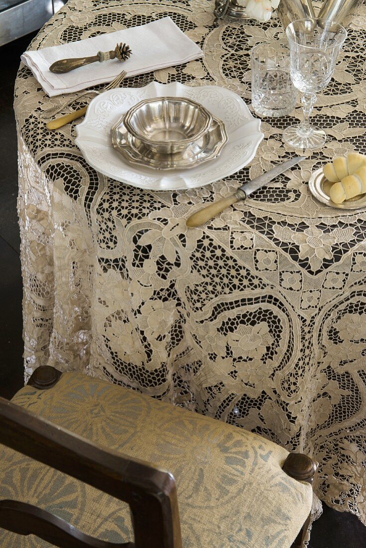 Lace tablecloth and vintage place setting next to upholstered chair