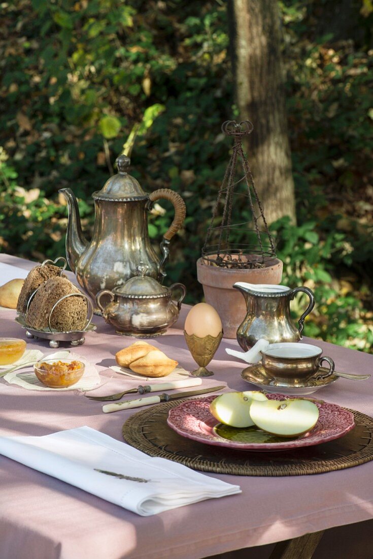 Gedeckter Frühstückstisch mit Silbergeschirr, Frühstücksei und Obstteller im Garten