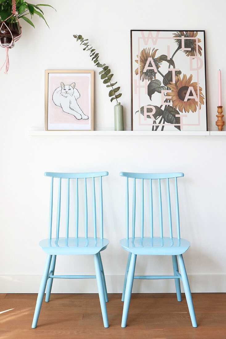 Two Windsor chairs painted pale blue below pictures on narrow shelf