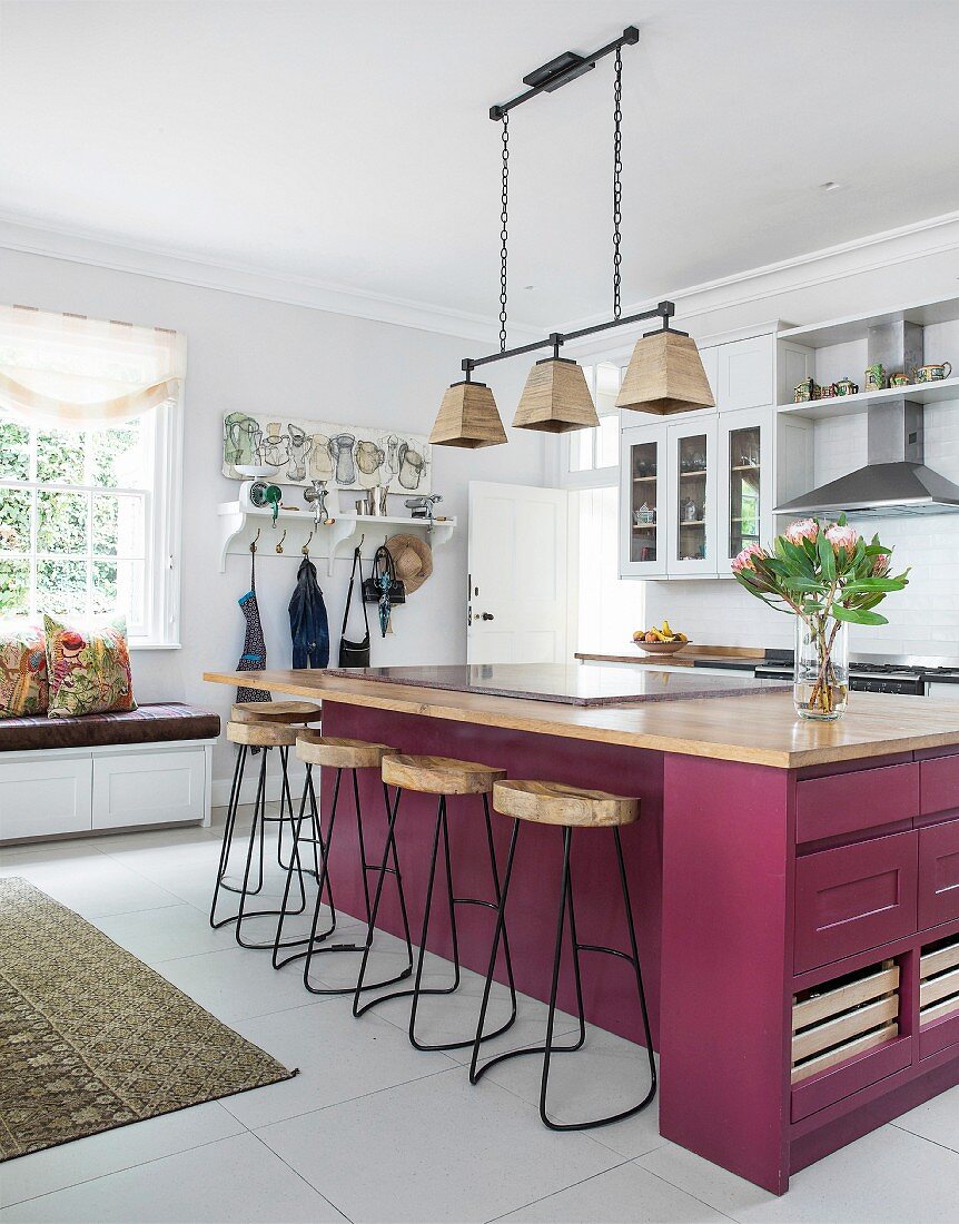 Berry-coloured island counter and delicate bar stools in bright kitchen