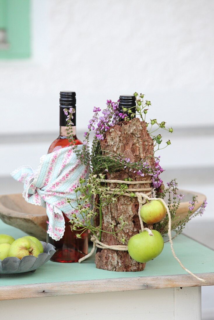 Herbstlich dekorierte Flasche, umwickelt mit Baumrinde, Heidekraut und festgebundenen grünen Äpfeln