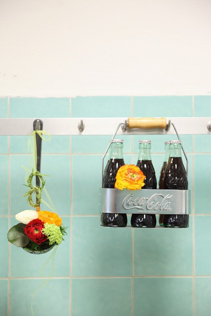 Schöpfkelle mit Blumen und Flaschenträger an einer Hakenleiste