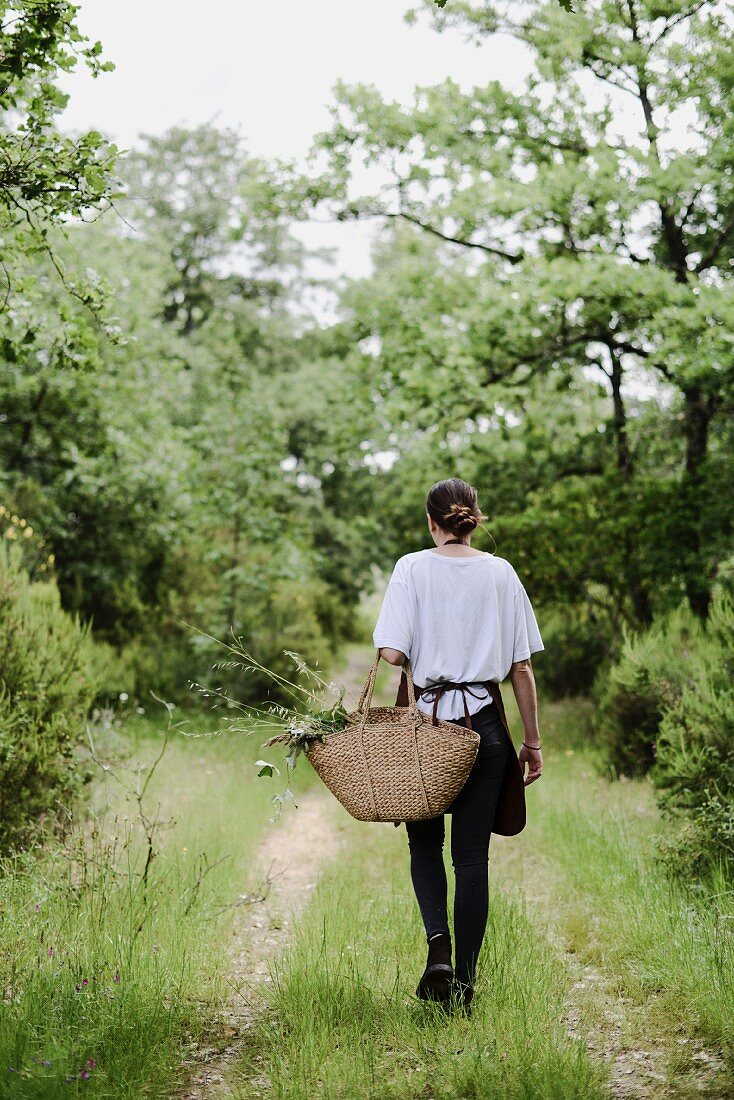 Frau mit Korbtasche geht auf einem Trampelpfad durch die Natur