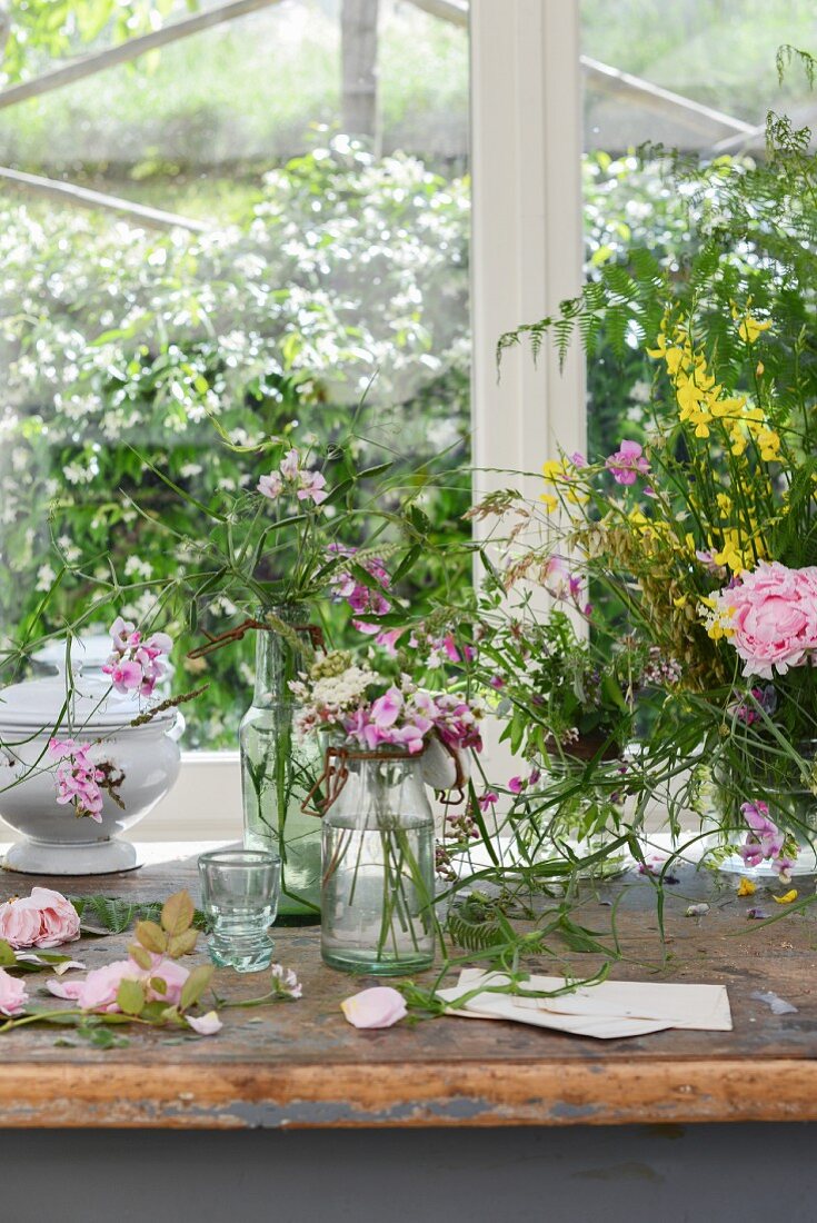 Vases of wildflowers on worn table below window