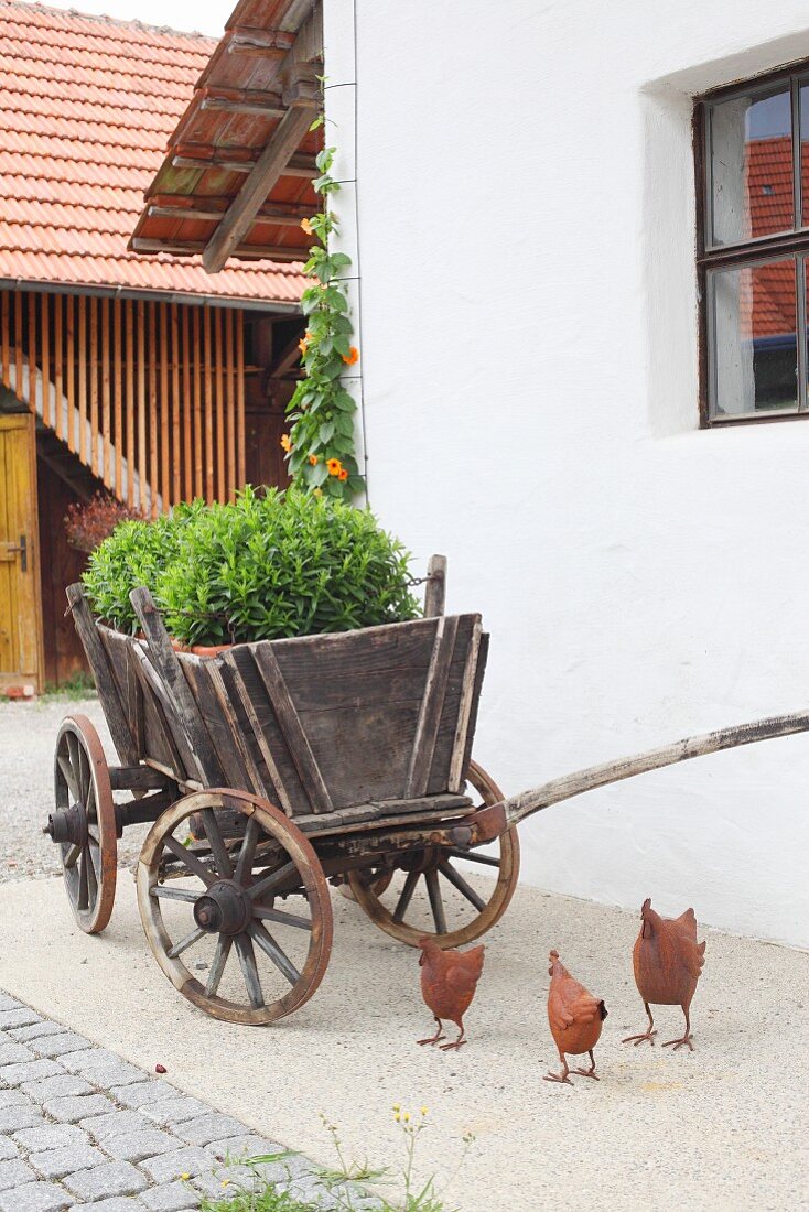Dekohühner aus Metall vor einem alten Holzkarren mit Pflanzen